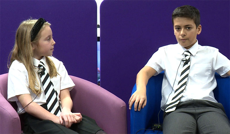 2 primary school sat in chairs wearing lapel mics