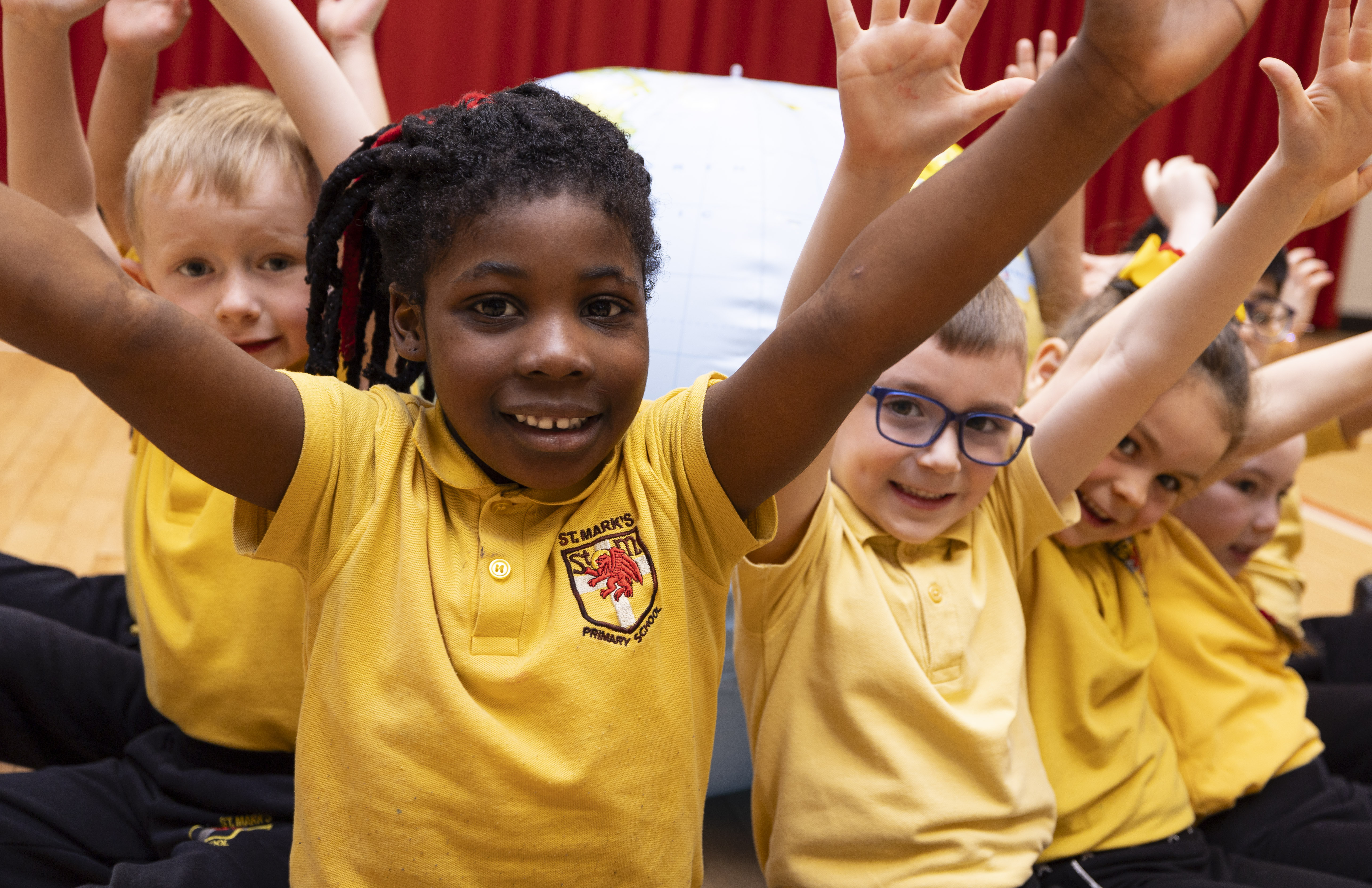 Young pupils wearing yellow t-shirts smiling and raising both arms in the air